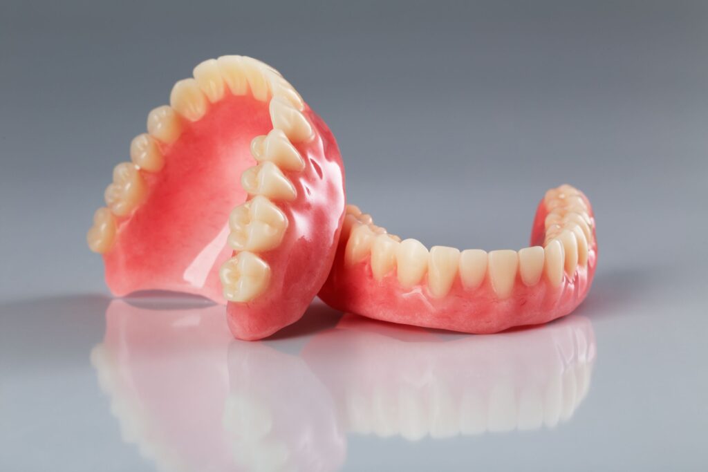 Upper set of dentures resting on a lower set on a reflective gray surface